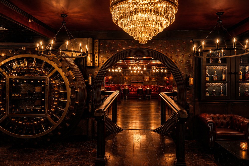 The open brass bank vault door at Bueno, framing a candlelit dining room beneath a crystal chandelier